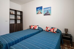 A room with two beds, a wooden wardrobe, a nightstand, and two wall-mounted pictures.