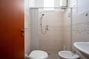 A bathroom with a shower, toilet, bidet, and sink.