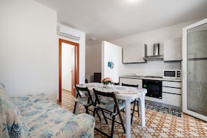 Een ruimtelijk ingerichte leefruimte met een eethoek, kitchenette en een bank met een gestreept hoesje.