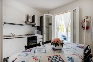 A compact kitchen with a microwave, stove, and cabinets, a dining table with a floral centerpiece, and a sliding glass door to a balcony.