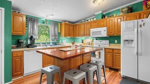 A kitchen with wooden cabinets, a central island with stools, a white refrigerator, and a microwave. - Atchley Hill Farm (Knoxville)