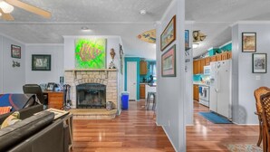 A living room with a fireplace, wooden flooring, and a kitchen in the background. - Atchley Hill Farm (Knoxville)
