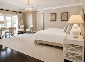 A spacious bedroom with a large bed, a sitting area with chairs, a dining table, and a chandelier. - Pelican Beach Mansion (Fort Lauderdale)