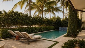 A pool area with lounge chairs, a small table, and a lantern. - Pelican Beach Mansion (Fort Lauderdale)