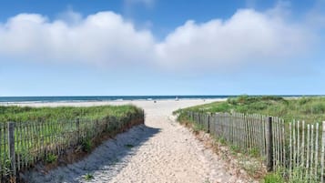 A sandy beach path leading to the ocean, flanked by wooden fences and grassy dunes.