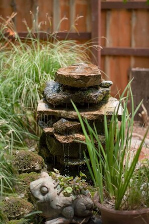 A tiered stone water feature with cascading water, surrounded by greenery and a wooden fence. - Rustic Cabin by Slide Rock - Sycamore (Sedona)