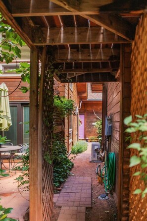 A narrow alleyway with a wooden pergola, brick pathway, and greenery.