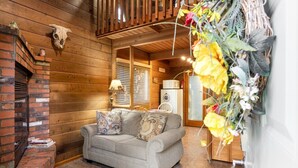 A cozy cabin interior with a fireplace, a sofa with patterned cushions, and a decorative wall hanging. - Rustic Cabin by Slide Rock - Sycamore (Sedona)