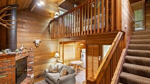 A cozy cabin interior with a fireplace, a sofa, a dining area, and a staircase. - Rustic Cabin by Slide Rock - Sycamore (Sedona)