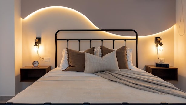 Ein ordentlich bezogenes Bett mit Kopfteil, zwei Nachttische mit Lampen und eine Klimaanlage an der Wand.