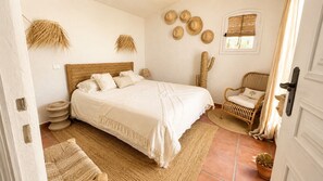 A bedroom with a large bed, a wicker chair, a cactus, and a window with blinds. - Villa la maison du Sud by Sea view property rental (les issambres)