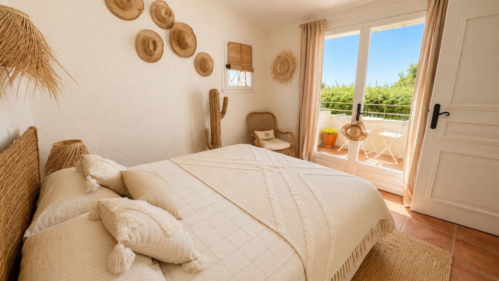 A bedroom with a bed, pillows, a chair, a cactus, and a balcony with a view.