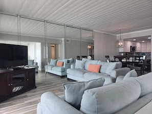 Ein modernes Wohnzimmer mit einem großen Flachbildfernseher, grauen Sofas, einem Holztisch und einer Glastrennwand.