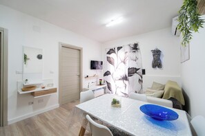 Ein modernes Wohnzimmer mit Esstisch, weißen Sofas, einem Fernseher und einer Zimmerpflanze.