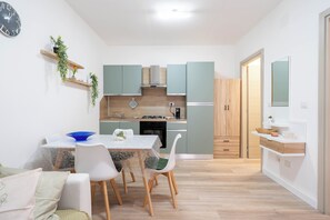 Eine moderne Küche mit hellgrünen Schränken, ein Essbereich mit weißen Stühlen und ein Holzboden.