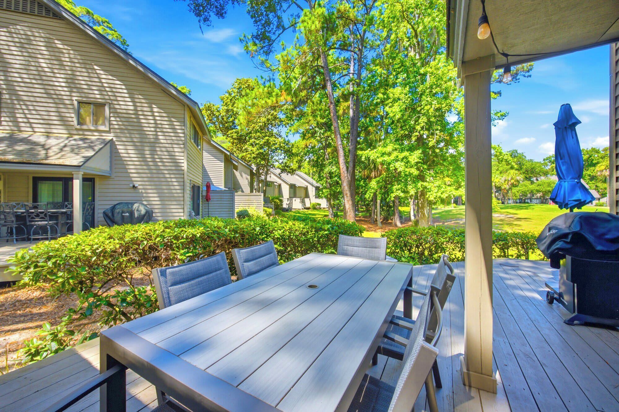 A covered outdoor patio with a table and chairs, surrounded by greenery and a view of a residential area.