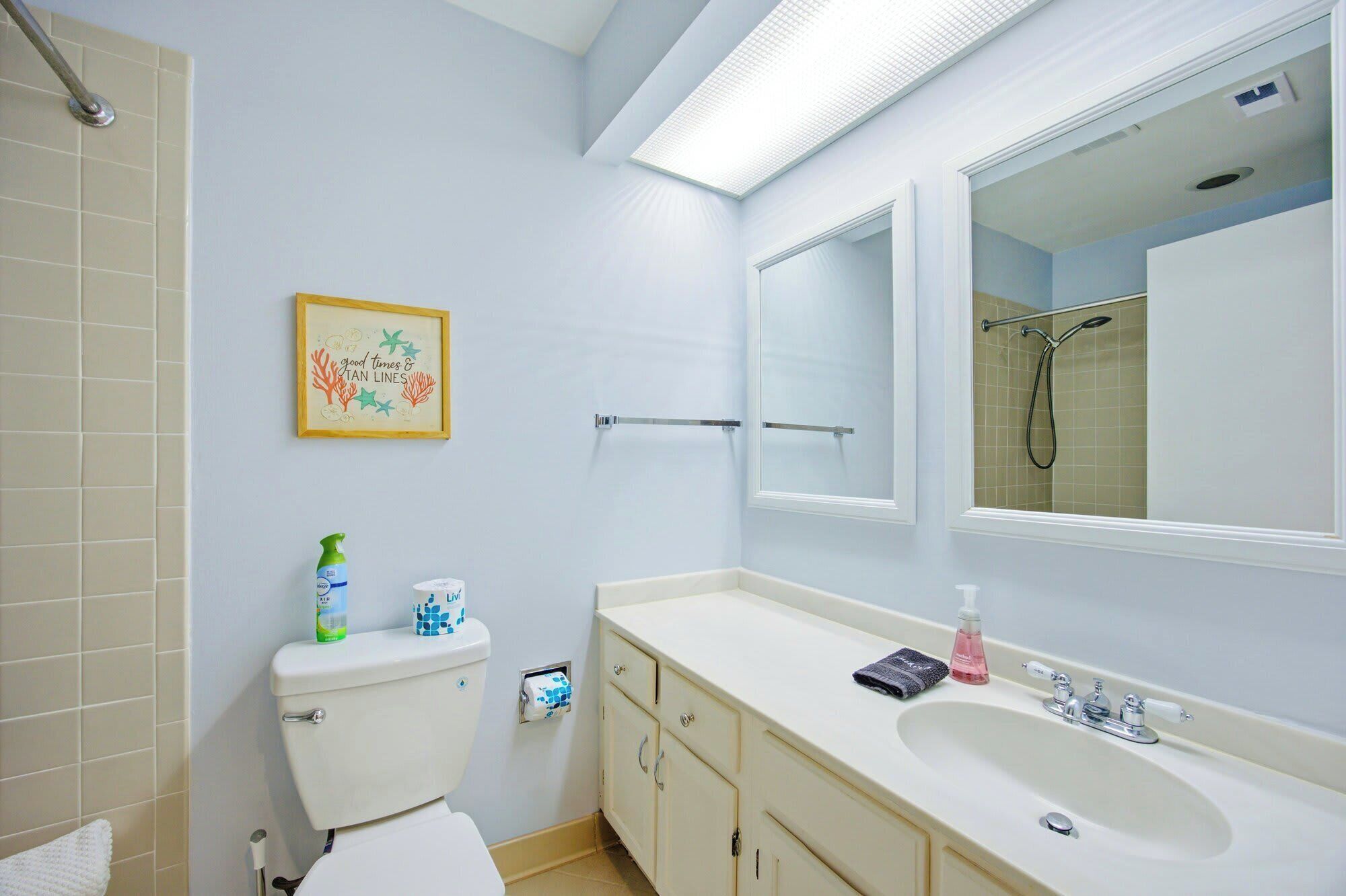 Une salle de bain comprenant des toilettes, un lavabo, un miroir, une douche et un tableau encadré au mur.