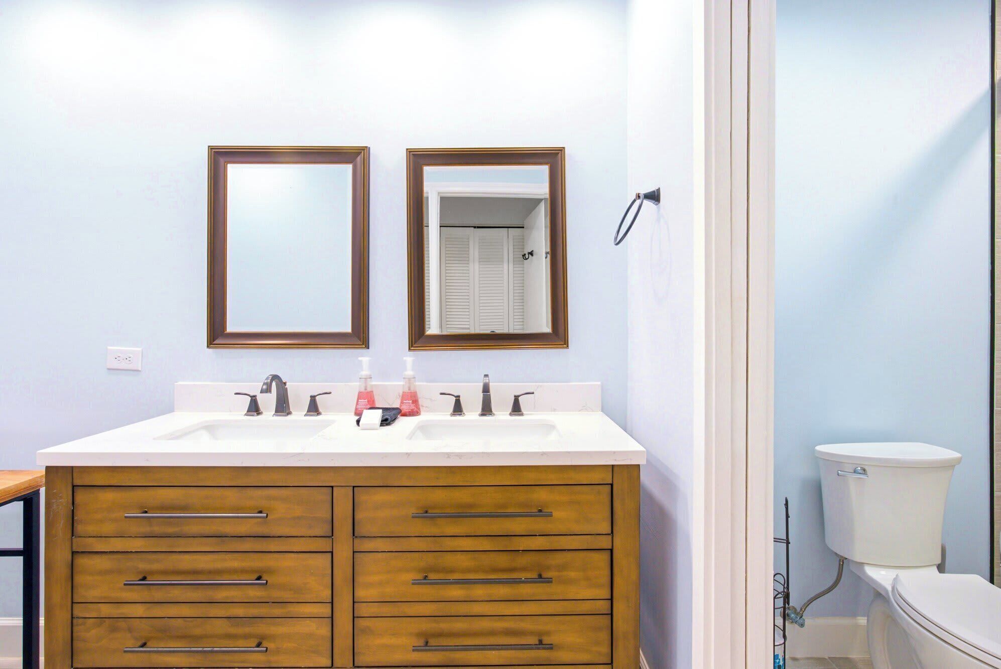 Warm wood cabinetry and crisp white stone create a clean, grounded space for your morning routine. Twin mirrors and soft lighting make this airy bathroom feel both expansive and intimate.
