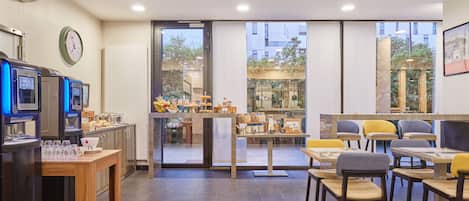 A modern cafe with a seating area, a coffee machine, and a view of the outside.