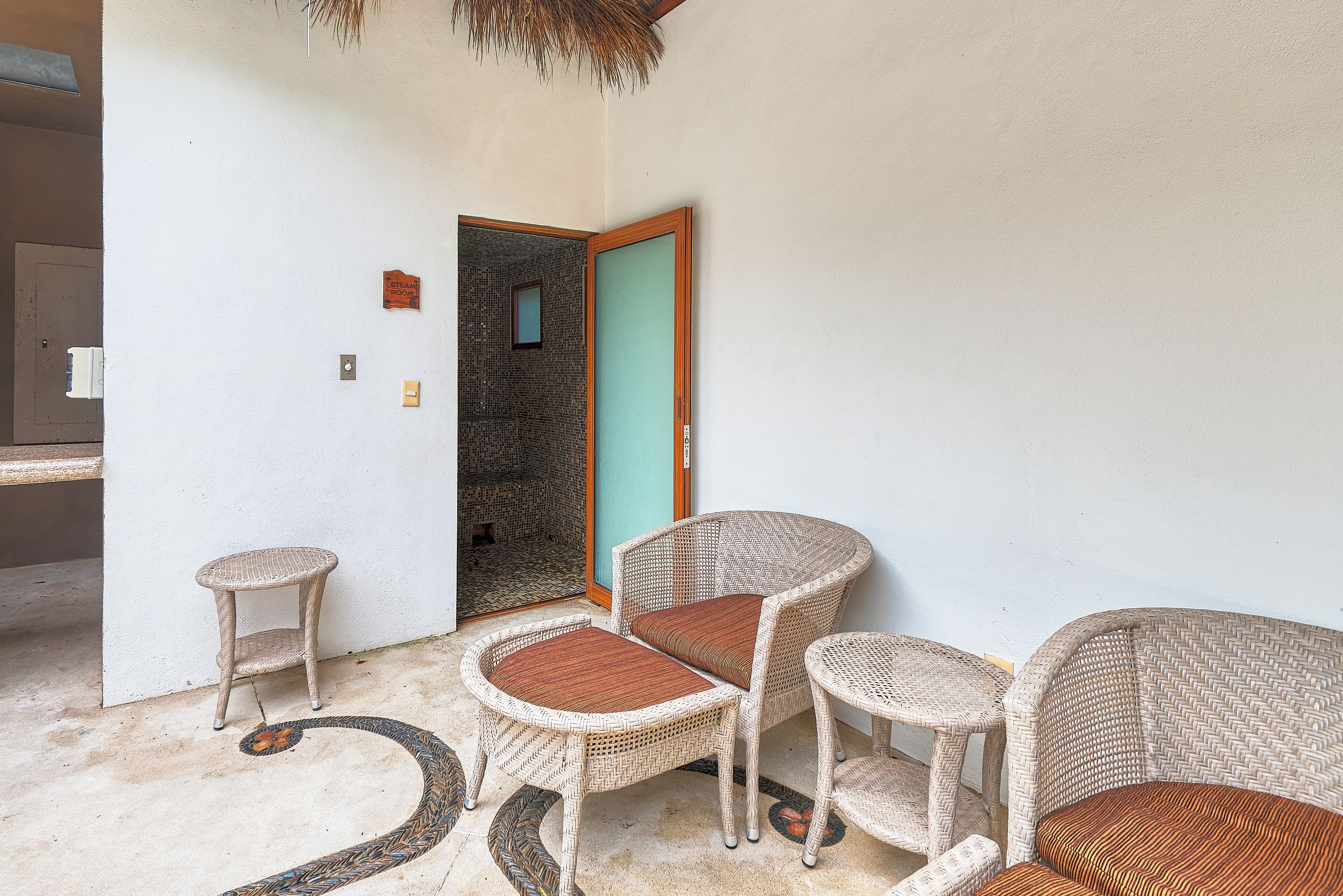 A room with wicker furniture, a door leading to a tiled area, and a small wall-mounted light.