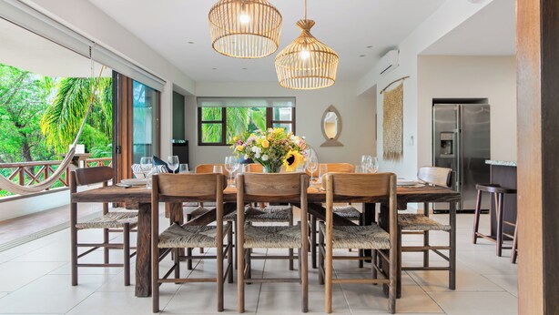 A dining area with a wooden table and chairs, a vase of flowers, and hanging wicker light fixtures. - Haixa Resort with Terrace in Punta Mita (Higuera Blanca)