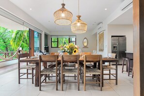 Un coin repas avec une table et des chaises en bois, un vase de fleurs et des luminaires suspendus en osier.