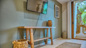A room with a wooden console table, a woven basket, a television mounted on the wall, and a framed artwork. - Haixa Resort with Terrace in Punta Mita (Higuera Blanca)