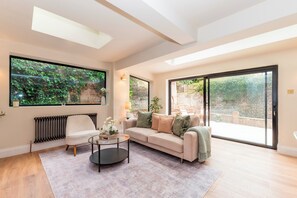 A spacious living room with a large window, a sofa, a coffee table, and a radiator. - Luxury 2BR Apartment, Garden & Central Access - Pass the Keys (London)