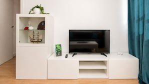 A modern living room with a flat-screen TV on a white entertainment unit, a small shelf with decorative items, and a door leading to another room. - Buleria: The Charm and Essence of Jerez (Jerez de la Frontera)