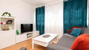 A modern living room with a flat-screen TV, white entertainment unit, grey sofa, and teal curtains. - Buleria: The Charm and Essence of Jerez (Jerez de la Frontera)