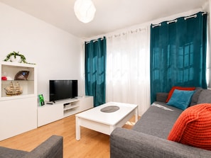 Ein modernes Wohnzimmer mit Flachbildfernseher, weißem Unterhaltungsschrank, grauem Sofa und blaue-Grün Vorhängen.