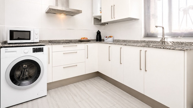 A modern kitchen with white cabinets, a built-in washing machine, a microwave, and a stainless steel range hood. - Buleria: The Charm and Essence of Jerez (Jerez de la Frontera)