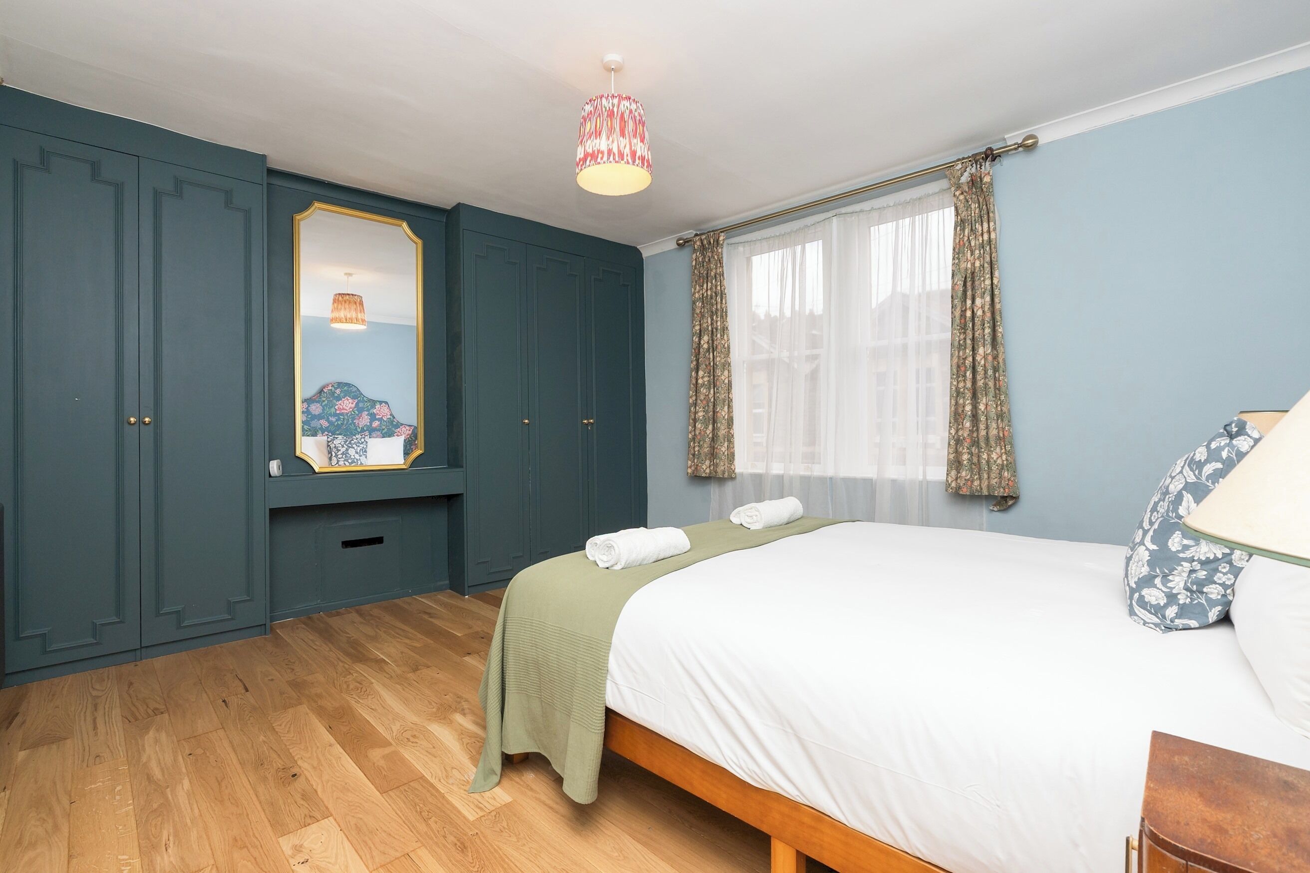 A bedroom with a bed, a mirror, a wardrobe, and a hanging light fixture.