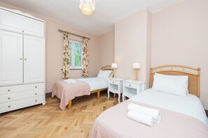 Ein Schlafzimmer mit zwei Betten, einem Kleiderschrank, einem Fenster mit Vorhängen, Nachttischen und einer Lampe.