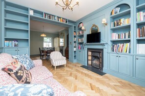 Ein Zimmer mit Kamin, Bücherregalen, einer Couch und einem Essbereich.