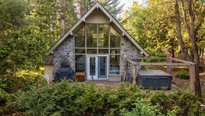 Een chalet met een stenen gevel, een glazen deur, een overdekte zithoek en een hottub.