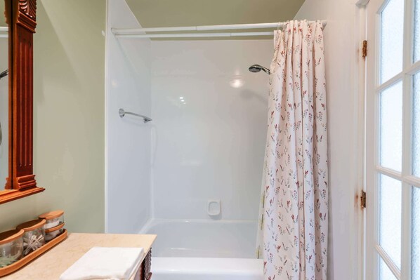 A bathroom with a shower, a mirror, and a window with a curtain.
