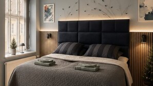 Un dormitorio con una cama, una ventana, un radiador y una lámpara fijada a la pared.