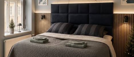 A bedroom with a bed, a window, a radiator, and a wall-mounted lamp.