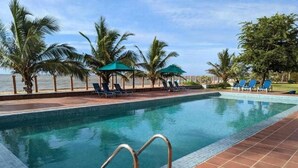 Une piscine dont le bord est revêtu de carrelage, entourée de chaises longues et de palmiers.