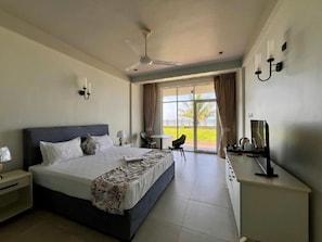 A hotel room with a bed, a desk, a TV, a ceiling fan, and a view of the outdoors.