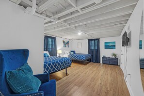 Une pièce avec deux lits, un canapé bleu, un plancher en bois et un plafond blanc avec des poutres apparentes.