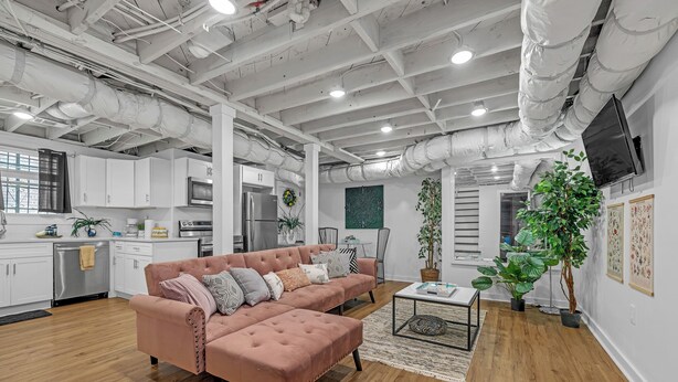 Et moderne interiør med synlige ventilationskanaler, en modulsofa, et sofabord og en stor plante.
