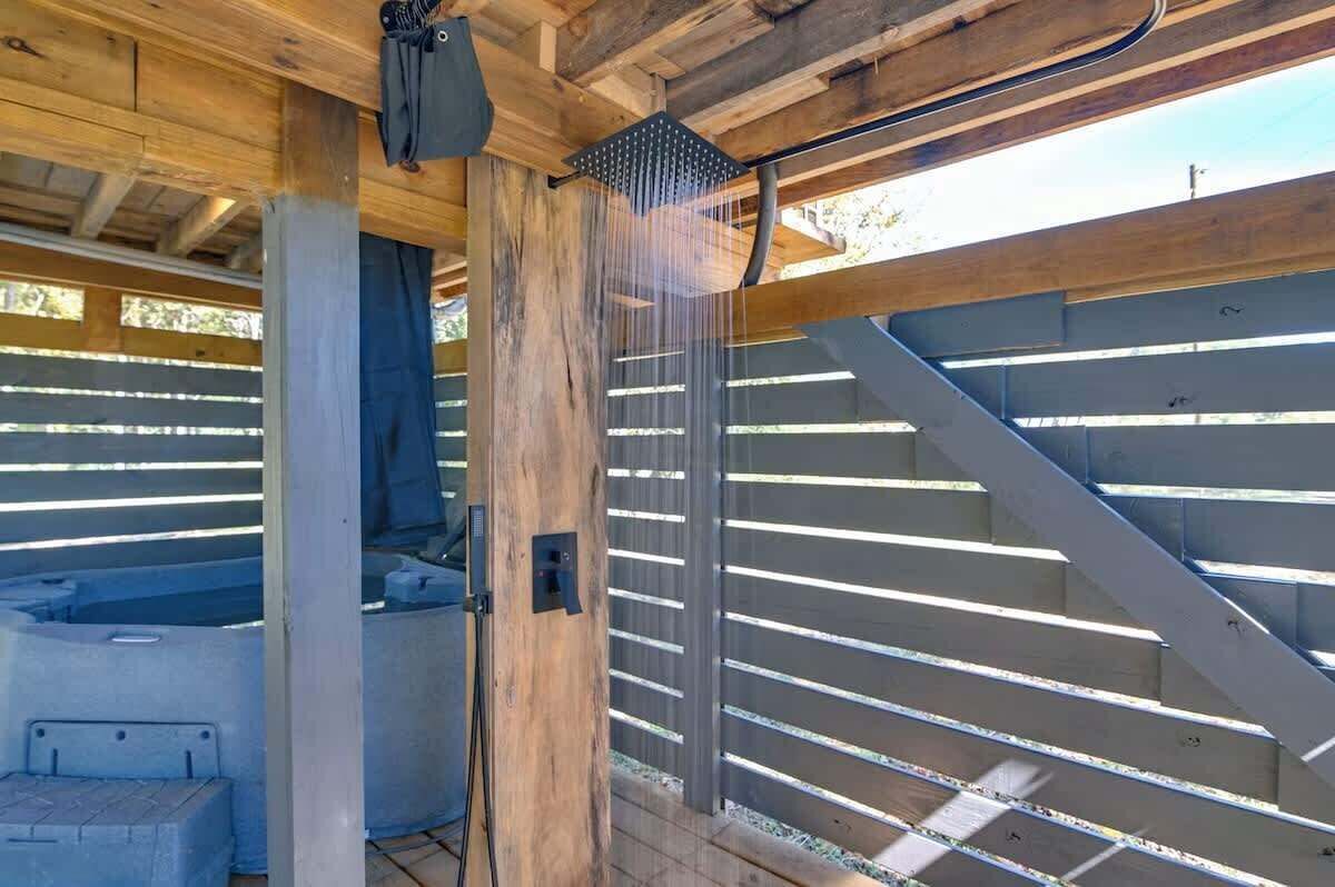 A wooden structure with a metal railing, a hot tub, and a shower area.