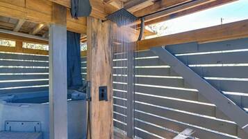 A wooden structure with a metal railing, a hot tub, and a shower area.