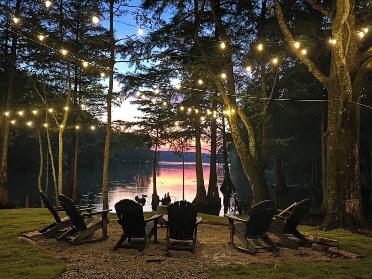 An outdoor seating area with chairs and tables, surrounded by trees and a view of a lake.