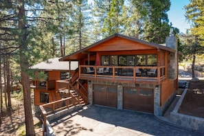 A two-story wooden cabin with a stone foundation, a balcony, and a garage. - Luna’s Mountain Manor | Chef Kitchen & Game Room (Stateline)
