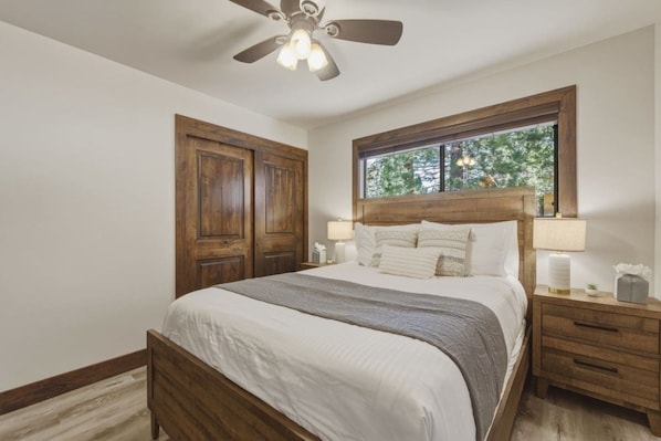 A bedroom with a wooden bed, a nightstand, a window with a view, and a ceiling fan. - Luna’s Mountain Manor | Chef Kitchen & Game Room (Stateline)