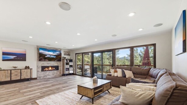 A modern living room with a fireplace, a leather sofa, and a large window overlooking a deck. - Luna’s Mountain Manor | Chef Kitchen & Game Room (Stateline)