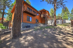 A two-story wooden cabin with a stone foundation, a wooden deck, and a fenced yard. - Luna’s Mountain Manor | Chef Kitchen & Game Room (Stateline)